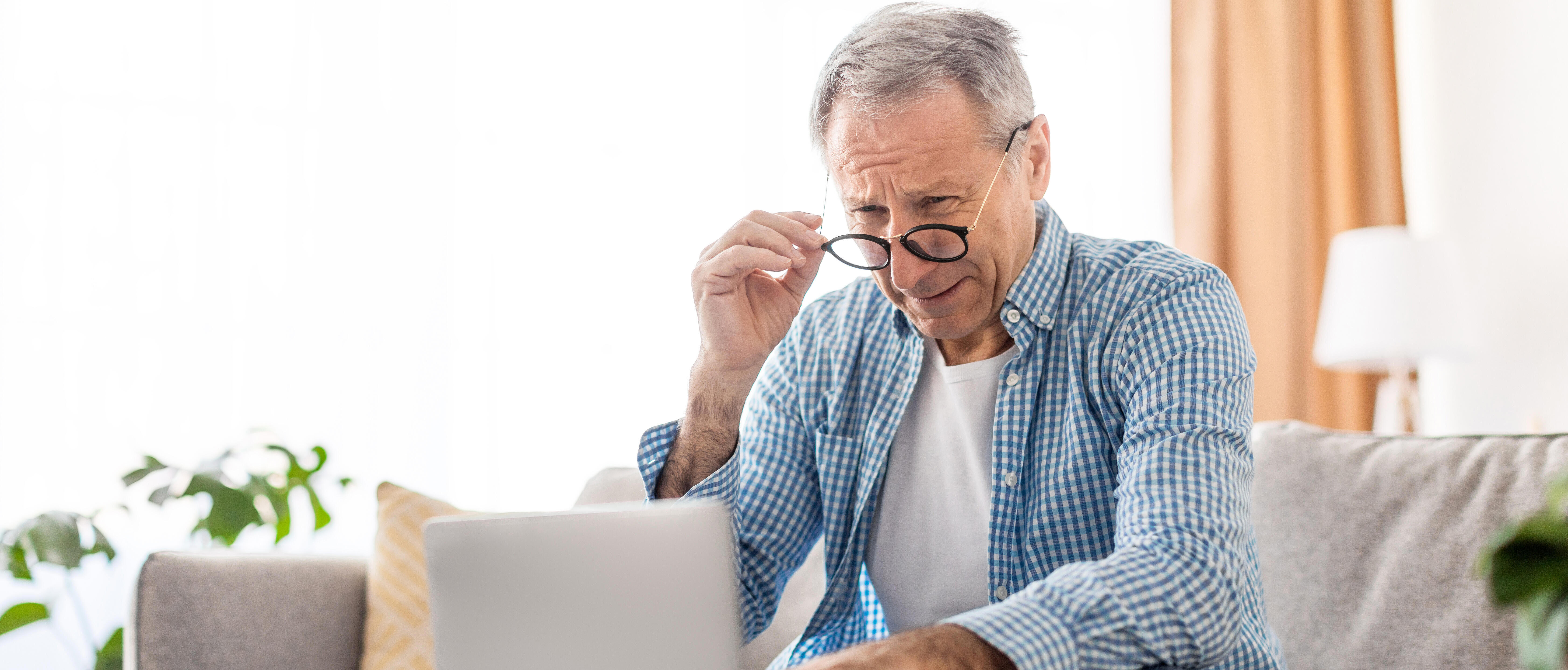 Mature man squinting using laptop, looking at pc screen