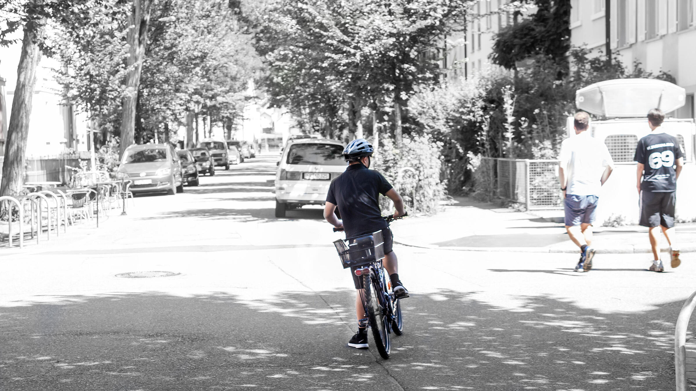 Ein Kind wartet darauf, mit dem Fahrrad die Straße zu überqueren, bis die Fußgänger aus dem Weg sind.
