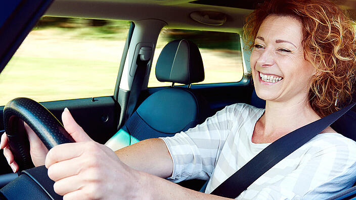 Happy female driver steering car with safety belt