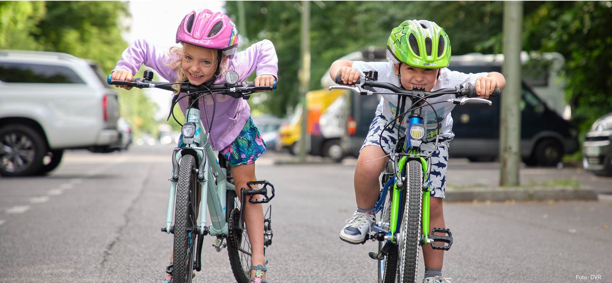 Ein Mädchen und ein Junge stehen an ihren Fahrrädern und lachen in die Kamera