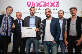Sechs Männer stehen nebeneinander, einer hält den Preis, eine Urkunde, hoch.