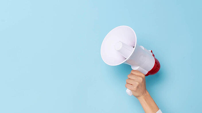 Business Hand holds a megaphone from a hole in the wall on blue background.  hiring, advertising, advertise and Banner concept.