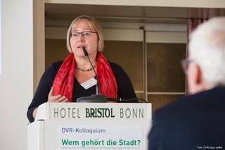 VCD-Bundesvorsitzende Kerstin Haarmann steht auf dem Podium hinter einem Pult. Die Aufnahme ist aus der Perspektive des auf Stühlen sitzenden Publikums gemacht.