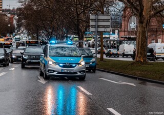 Ein blau-weißes Polizeiauto fährt auf einer dreispurigen Straße. Hinter ihm fahren Busse und weitere Pkw.