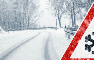 Eine schneebedeckte Landstraße und das Verkehrszeichen für Schneefall