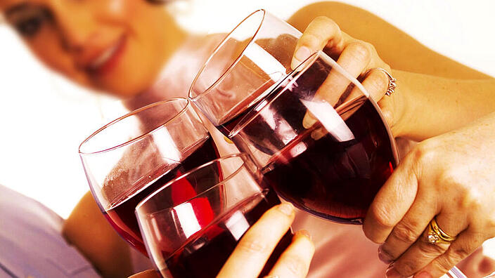 Eine Frau und weitere Personen stoßen mit Rotwein an