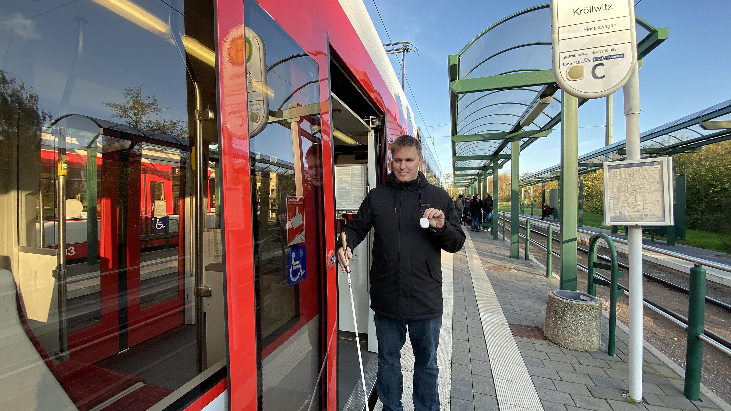 Ein Mann mit Blindenstock und Transponder steht an der Tür einer Straßenbahn