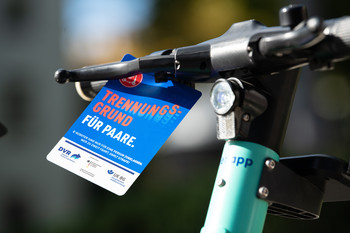 Am Lenker eines E-Scooters hängt ein Flyer der Kampagne Roll ohne Risiko
