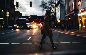 Eine Fußgängerin in dunkler Kleidung überquert die Straße. Es ist dunkel.