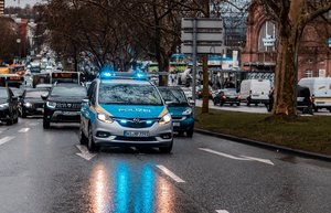 Ein blau-weißes Polizeiauto fährt auf einer dreispurigen Straße. Hinter ihm fahren Busse und weitere Pkw.