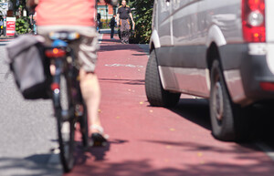 Eine Frau fährt auf einem roten Radschutzstreifen und wird knapp von einem Kleintransporter überholt