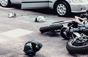 Ein Motorrad liegt rexhts vor einem grauen Pkw. Neben dem Motorrad liegen ein Helm sowie verschiedene Motorradteile.