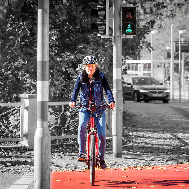 Eine Frau mit  Fahrradhelm überquert bei grün die Straße auf dem Fahrrad.