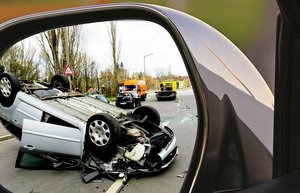 Durch den Seitenspiegel eines Autos richtet sich der Blick nach hinten auf einen Verkehrsunfall. 