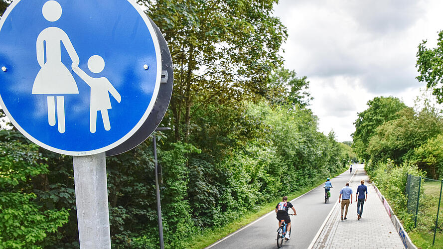 Links Radfahrende auf der Veloroute, rechts daneben der Fußweg mit zu Fuß Gehenden, vorne im Bild das Verkehrszeichen 239 "Gehweg".
