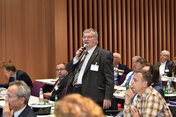 Ein Mann steht mit einem Mikrofon hinter einem Konferenztisch