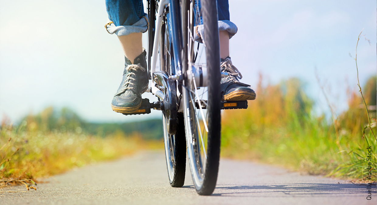 Eine Person fährt auf einem Feldweg, wobei nur die untere Hälfte vom Fahrrad und der Person abgebildet sind.